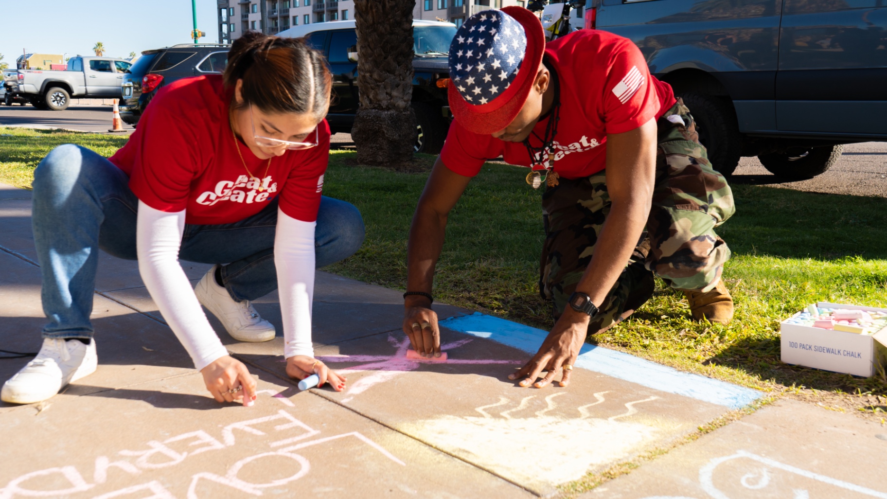 Two members drawing sidewalk chalk art in Be Great & Create shirts