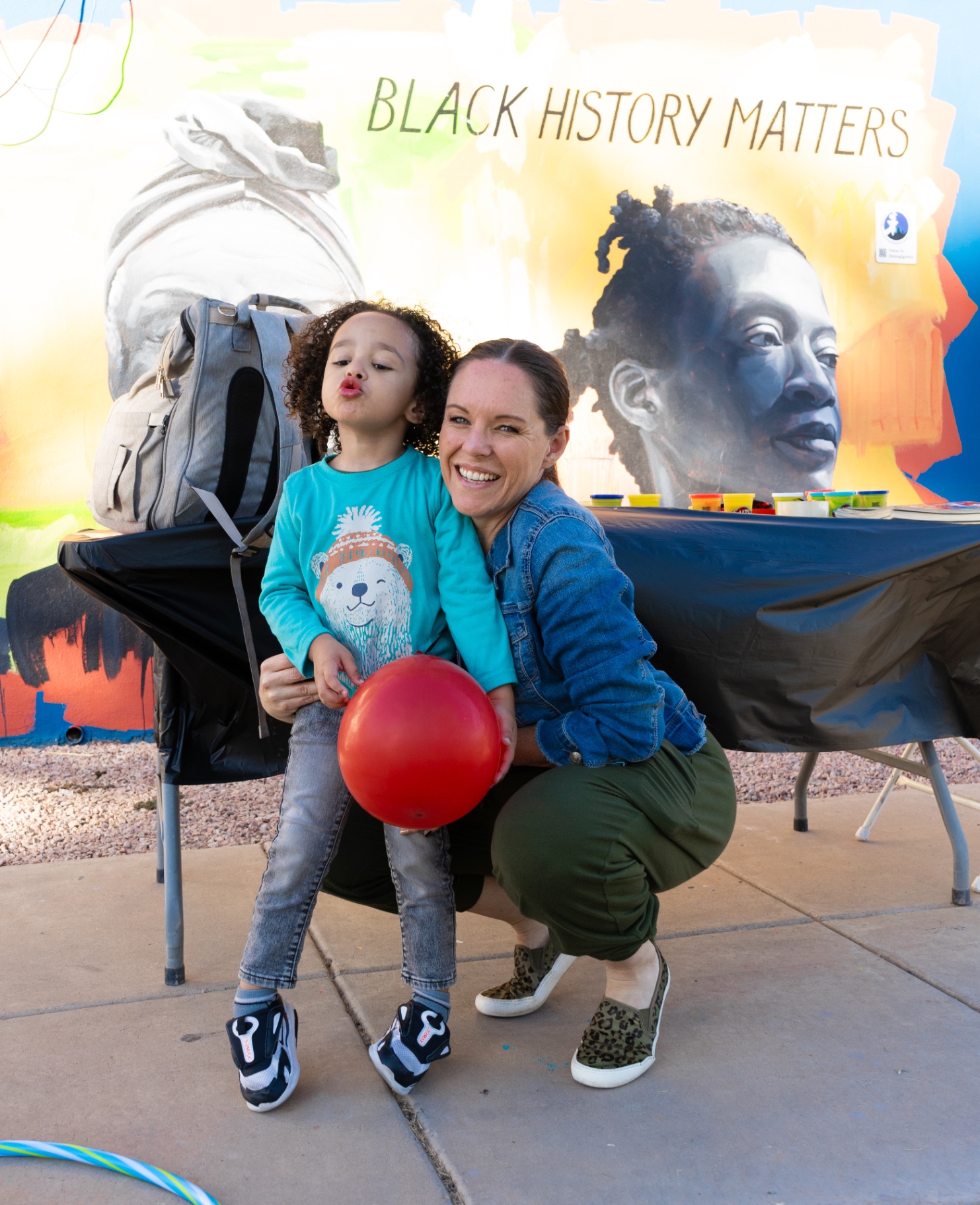 A volunteer and a child smiling in front of a community mural